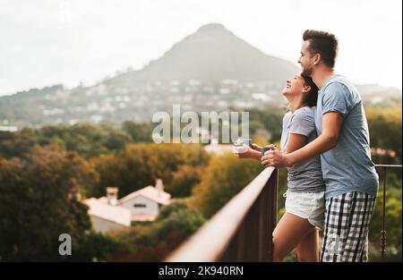 Portiamo pace e felicità nelle vite degli altri. Una giovane coppia affettuosa beve caffè mentre si alza in piedi sul balcone di casa nel Foto Stock