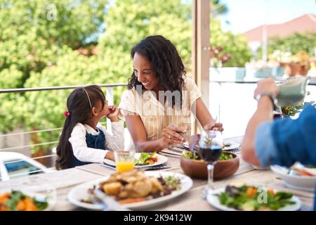 Condividiamo un legame speciale tra noi: Una bambina adorabile e sua madre che si divertono durante un pasto con la famiglia all'aperto. Foto Stock