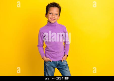 Ritratto fotografico di incantevole bambino braccia tasche autunno inverno collezione indossare abiti viola alla moda isolato su sfondo giallo Foto Stock