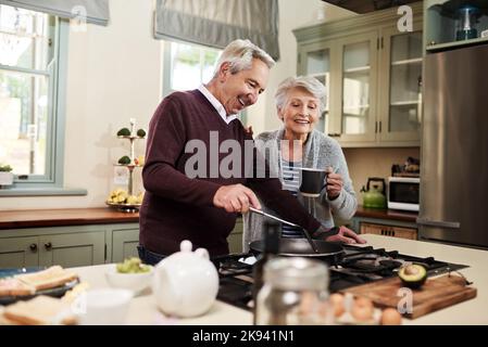 Ha piena fiducia nelle mie abilità culinarie. Una coppia anziana affettuosa che cucinava insieme nella loro cucina a casa. Foto Stock