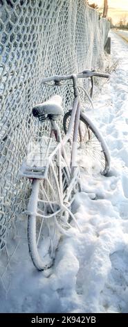 Panorama verticale di una bicicletta innevata appoggiata contro una recinzione a lato di una strada Foto Stock