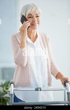 Im che fa bene caro e voi. Una donna anziana felice che prende una telefonata mentre usando un camminatore in una casa di pensione. Foto Stock