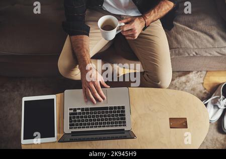 Grazie alla tecnologia, non avrete mai giornate noiosi a casa vostra. Ripresa ad alto angolo di un uomo irriconoscibile utilizzando il suo notebook mentre si rilassa sul divano a casa. Foto Stock