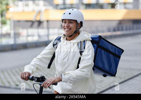 Ritratto di sorridente addetto alla consegna di cibo che indossa il casco mentre si guida su uno scooter elettrico Foto Stock