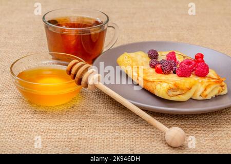 Frittelle fatte in casa con miele in una ciotola e una tazza di tè Foto Stock