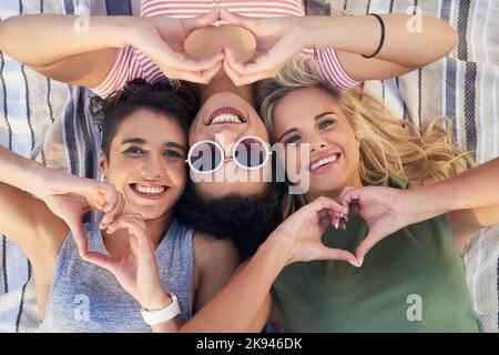 Ci piace tanto l'estate quanto gli amiamo gli altri: Tre amici che si trovano insieme su una coperta da picnic. Foto Stock
