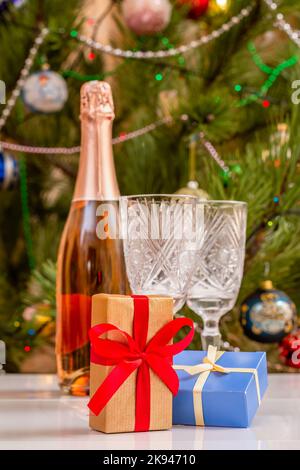 Scatole regalo e bicchieri di cristallo sfocati, bottiglia di champagne e albero di Natale con luci scintillanti e palle giocattolo. Foto Stock