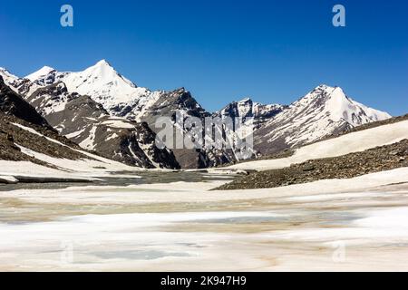 Vette innevate dell'Himalaya sotto un cielo blu sopra un lago ghiacciato vicino al passo d'alta quota di Shingo la a Zanskar. Foto Stock