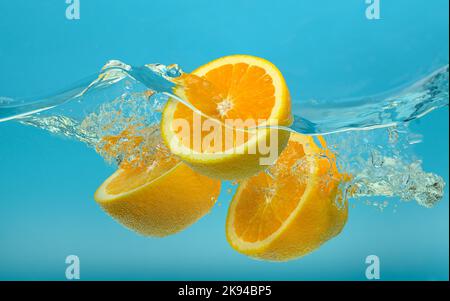 Le metà arancioni fresche cadono in acqua con spruzzi su sfondo blu. Foto Stock