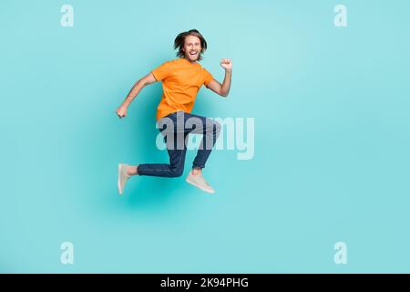 Foto a tutta lunghezza di sicuro uomo eccitato indossare t-shirt arancione salto alta corsa veloce vuoto spazio isolato colore turchese sfondo Foto Stock