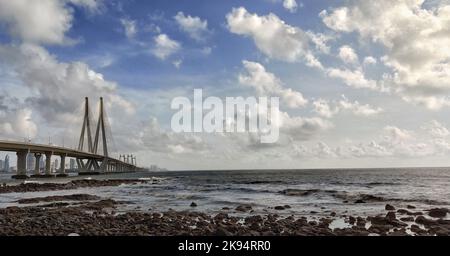 Vista dal basso del ponte di Bandra Worli Sea link attraverso la spiaggia rocciosa sotto le nuvole soffici, Mumbai, India Foto Stock