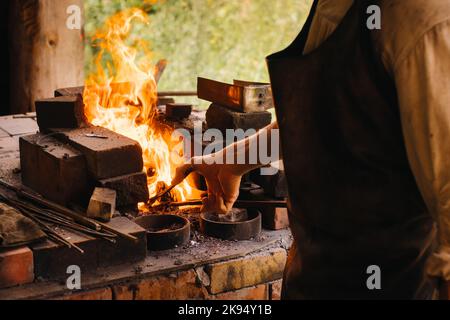 Un fabbro indurisce l'acciaio ad alta temperatura in una fornace fatta in casa nel villaggio Foto Stock