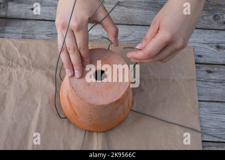 realizzazione di un dispenser per il materiale di nidificazione per uccelli o scoiattoli, fase 3: l'estremità libera del filo viene piegata attorno ad un vaso da fiori, figura 3/5 Foto Stock