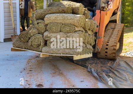 Durante le costruzioni, il carrello elevatore a forche con braccio scarica i pallet dei rotoli di erba sintetica verde per utilizzarli per l'architettura paesaggistica. Foto Stock