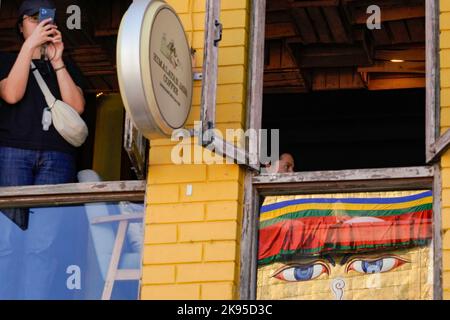 Kathmandu, Nepal. 26th Ott 2022. Una donna scatta una foto da un ristorante mentre le persone con disabilità e disabilità ballano e cantano alla canzone dei Deusi Bhailo, cantata per fortuna, gioia, E la felicità tra le persone durante il festival Tihar, noto come Diwali, il festival delle luci a Boudhanath Stupa, un sito patrimonio dell'umanità dell'UNESCO a Kathmandu. Un team di tredici persone diversamente abili ha iniziato i 3 giorni di Deusi Bhailo evento musicale per la consapevolezza sociale e il significato del grande festival indù nella società, con i desideri di tutti i nepalesi in tutto il mondo. Foto Stock