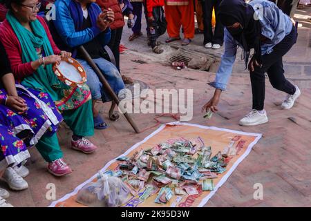 Kathmandu, Nepal. 26th Ott 2022. Una donna sostiene schizzando in denaro a persone con disabilità e disabilità mentre ballano e cantano la canzone Deusi Bhailo, cantata per buona fortuna, gioia, E la felicità tra le persone durante il festival Tihar, noto come Diwali, il festival delle luci a Boudhanath Stupa, un sito patrimonio dell'umanità dell'UNESCO a Kathmandu. Un team di tredici persone diversamente abili ha iniziato i 3 giorni di Deusi Bhailo evento musicale per la consapevolezza sociale e il significato del grande festival indù nella società, con i desideri di tutti i nepalesi in tutto il mondo. Foto Stock