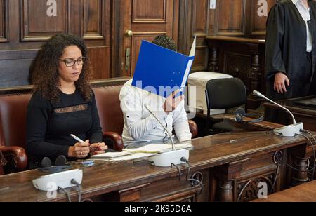 Amburgo, Germania. 26th Ott 2022. L'imputato (r) siede accanto a un interprete nella sala del tribunale prima dell'inizio del processo, tenendo una cartella blu davanti al suo volto. Il bambino di 27 anni è sottoposto a un processo per tentato massacro. Si dice che il convenuto abbia ferito fatalmente il suo partner con un coltello nell'ottobre 2021. Fuggì attraverso i tetti adiacenti e fu arrestato a Parigi il 11 novembre 2021, con un mandato d'arresto internazionale, e trasferito in Germania. Credit: Georg Wendt/dpa/Alamy Live News Foto Stock