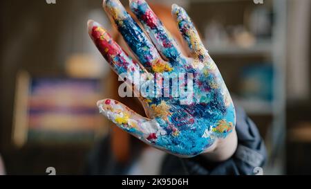Donna con capelli rossi caucasici artista designer ragazza pittore mostra sporco in pitture palmo colorato a macchina fotografica tenendo la mano di fronte al suo volto vicino con il braccio Foto Stock