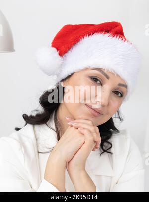 La giovane donna di successo indossa il cappello di natale di babbo Natale sull'ufficio di bellezza dello sfondo. Ritratto professionale estetista o manager e vacanze invernali Foto Stock