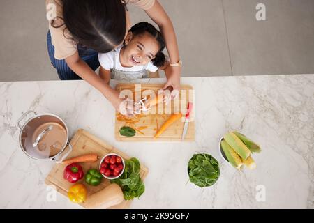 Sviluppo, bambino e madre in cucina, verdure e imparare la cucina insieme essere felici, sorriso e sicurezza. Vista dall'alto, cibo da peeling per mamma e ragazza Foto Stock