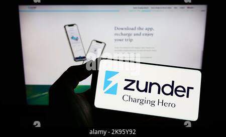 Persona che tiene il telefono cellulare con il logo della società spagnola Grupo Easycharger SL (Zunder) sullo schermo di fronte alla pagina web. Messa a fuoco sul display del telefono. Foto Stock