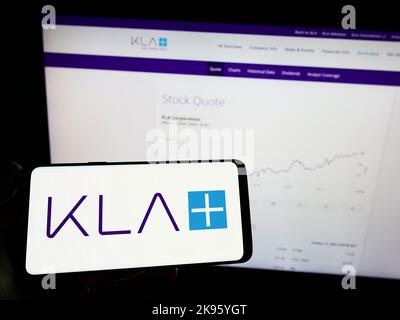 Persona che tiene il telefono cellulare con il logo della società americana di semiconduttori KLA Corporation sullo schermo di fronte alla pagina web. Messa a fuoco sul display del telefono. Foto Stock
