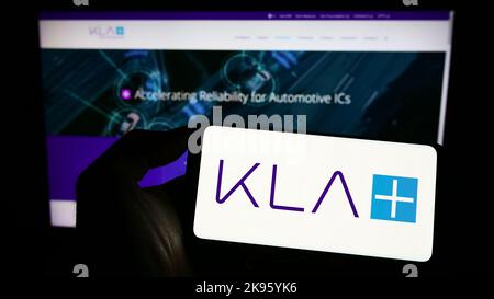 Persona che tiene in mano uno smartphone con il logo della società statunitense KLA Corporation sullo schermo di fronte al sito Web. Messa a fuoco sul display del telefono. Foto Stock