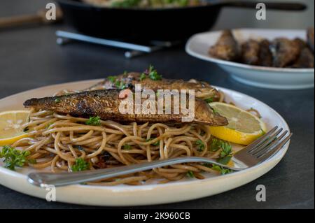 Spaghetti fatti in casa aglio e olio con sardine fritte su un piatto. Cotto con pasta di grano integrale Foto Stock