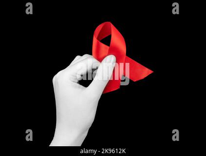 Nastro rosso in mano su sfondo nero per la giornata di sensibilizzazione sull'HIV AIDS, 1 dicembre. Foto di alta qualità Foto Stock