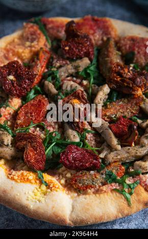Primo piano di una deliziosa pizza al tofu con pomodori secchi e rucola. Cibo vegano Foto Stock