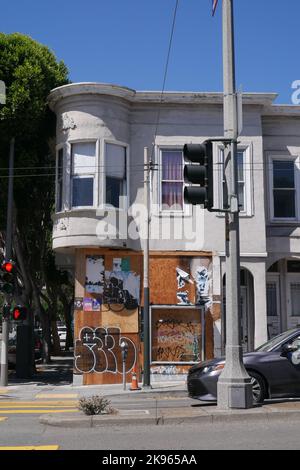 Un edificio a due piani con un fronte negozio al piano terra che e' stato imbarcato e coperto con graffiti e poster a San Francisco, California 2022 Foto Stock