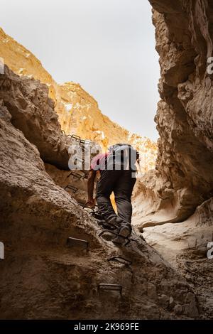 escursionista utilizzando pioli per salire su una roccia in un canyon del deserto Foto Stock