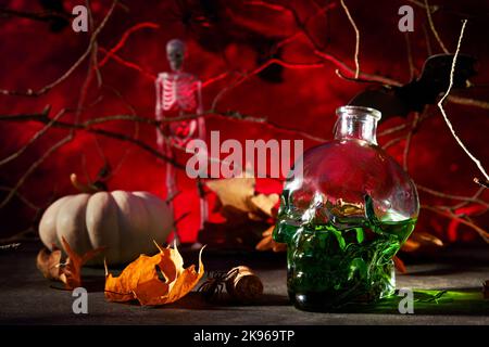 Cocktail verde di Halloween. Calice di vetro da cocktail di Halloween per Halloween e cranio a forma di bottiglia su sfondi scuri rossi. Festa di Halloween con occhi dolci Foto Stock
