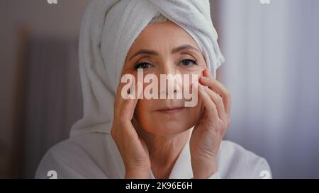 Primo piano ritratto felice signora anziana con anti rughe pelle idrogel collagene patch sotto gli occhi sorridendo alla macchina fotografica vecchia 60s donna caucasica con asciugamano Foto Stock