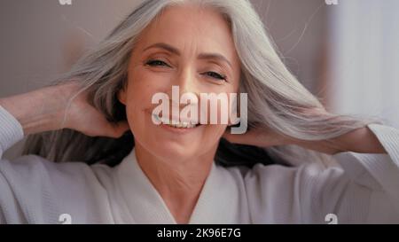 Splendida bella 60s vecchia di mezza età matura donna caucasica nonna anziana 50s donna sorridente guardando la macchina fotografica a casa coccole toccare grigio Foto Stock