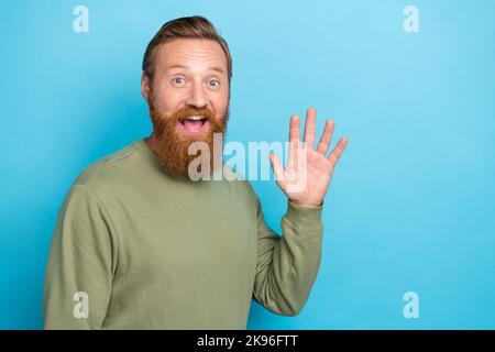 Foto di sincero ottimista positivo ragazzo con zenzero hairdo usura cachi manica lunga ondulazione palma dire hi isolato su sfondo di colore blu Foto Stock