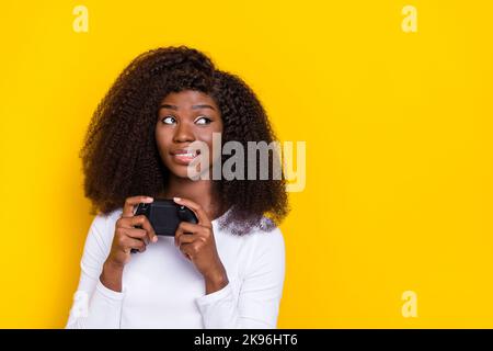 Ritratto di ragazza graziosa tenuta gamepad mordente labbra guardare spazio vuoto isolato su sfondo giallo colore Foto Stock