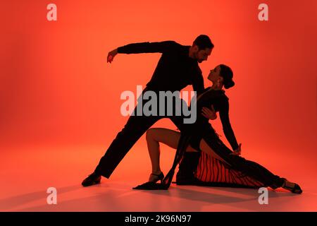 Vista laterale della ballerina professionista che abbraccia la donna in abito su sfondo rosso Foto Stock