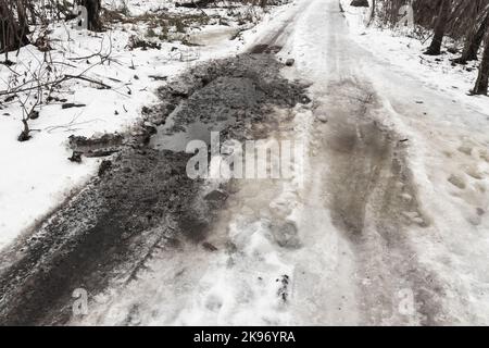 Strada rurale umida e sporca con neve e pozzanghere, foto di sfondo del trasporto Foto Stock