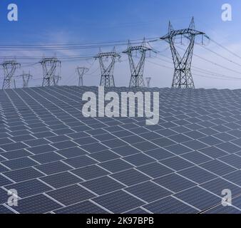 Pannelli solari con piloni ad alta tensione su cielo blu, impianto di produzione di energia elettrica con grande superficie di pannelli solari Foto Stock