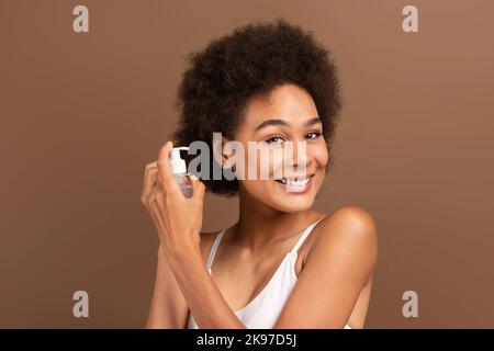 Allegro giovane misto razza femmina applicando gel sui capelli ricci, fare nuovo taglio di capelli, guardando la macchina fotografica Foto Stock