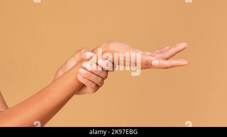 Primo piano di braccia femminili che tengono un polso doloroso, in piedi su sfondo beige studio, panorama, tagliato Foto Stock