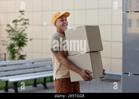 Ritratto di sorridente addetto alla consegna che tiene una pila di scatole accanto alla porta della casa Foto Stock