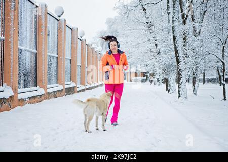 Come affrontare i cani randagi mentre si corre all'aperto. Corsa e jogging e cani da strada. Runner donna incontro cane randagio in inverno parco nevoso, foresta. Foto Stock