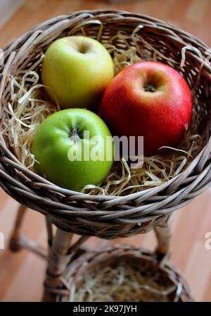 Frutti di mela freschi e colorati di diverse varietà in Un cesto di vimini con trucioli di legno su una rastrelliera di rattan Foto Stock