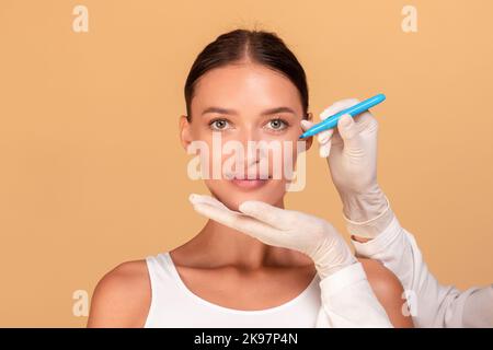 Signora prima di un intervento di chirurgia plastica. Estetista che tocca e disegna linee di correzione sul volto femminile Foto Stock