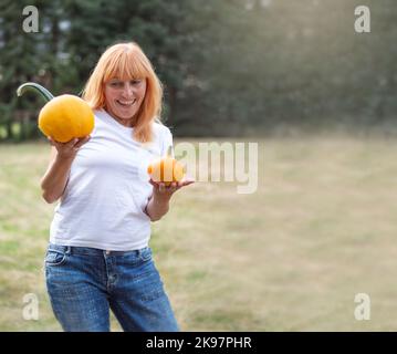 Giorno del Ringraziamento. Una ragazza in una t-shirt bianca tiene zucche ed è sorpreso, gioisce. Banner. Spazio di copia Foto Stock