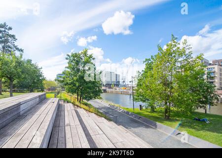 Gradini in legno e posti a sedere vi invitano a riposarvi nel Baakenpark di Amburgo. Il cielo blu è punteggiato di nuvole, gli alberi e i prati brillano di verde fresco. Foto Stock