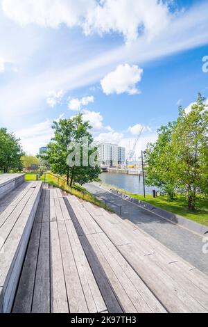 Gradini in legno e posti a sedere vi invitano a riposarvi nel Baakenpark di Amburgo. Il cielo blu è punteggiato di nuvole, gli alberi e i prati brillano di verde fresco. Foto Stock