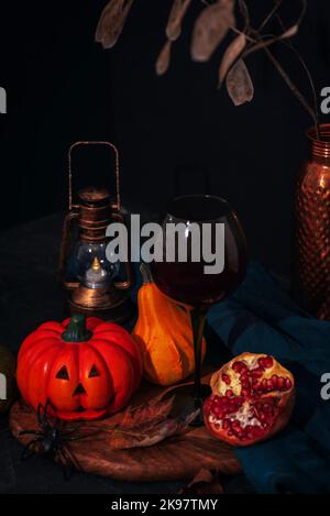 Allestimento festivo di Halloween con Jack-o-Lantern, zucche, lanterna d'annata, vino in un bicchiere e ragno sul tagliere in legno. Sfondo nero. Autunno Foto Stock